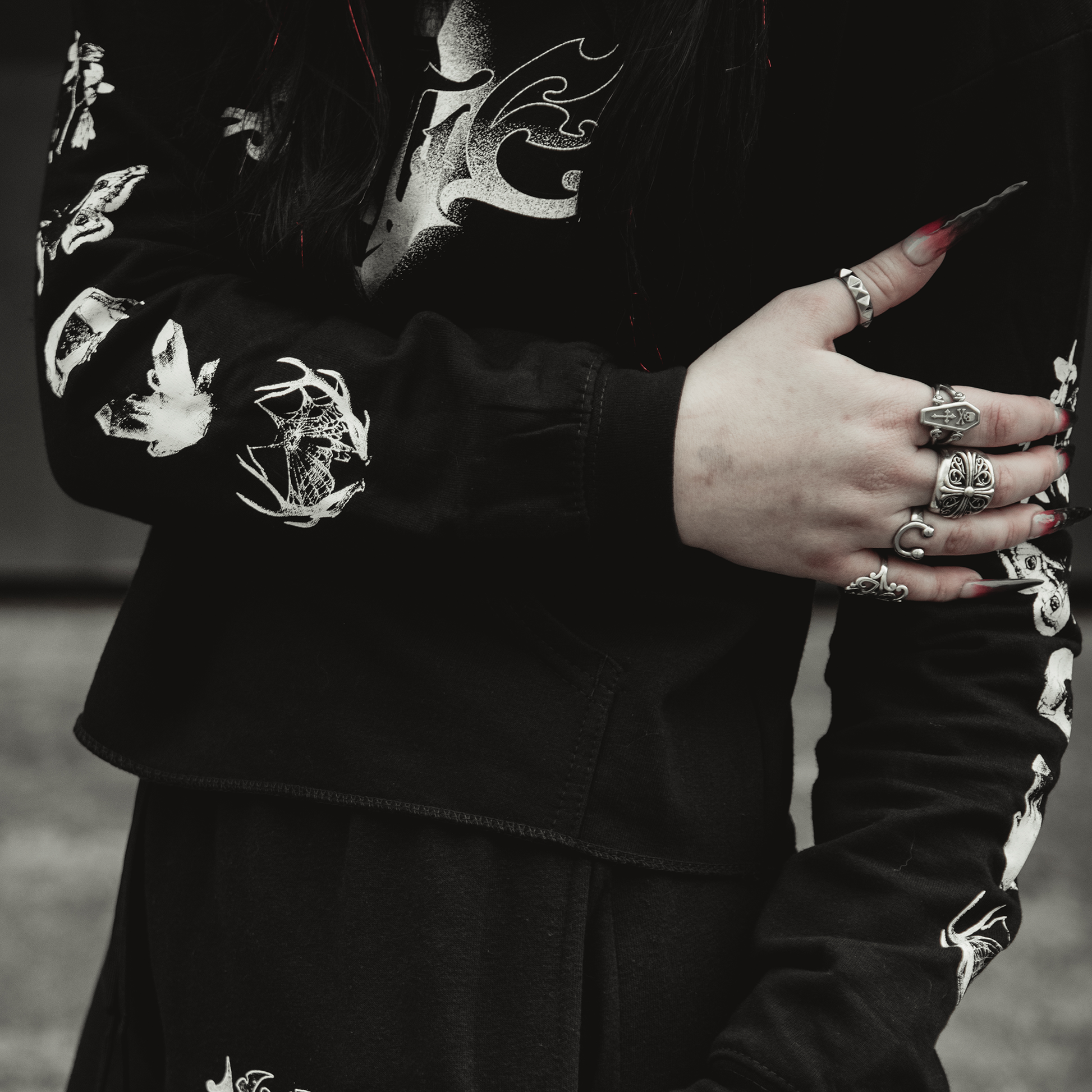 A person wears the Kittie Nox black cropped women's pullover, crossing their arm to show silver rings and long painted nails against a blurred background.
